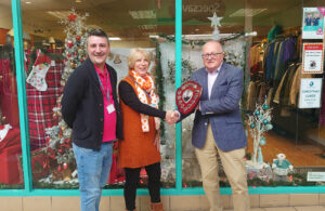 Photo of Best Christmas Shop Window Display competition winner 2022 St Wilfrids Hospice receiving award plaque. Pictured are shop deputy manager Graham Wellock with shop manager Heather Reece and Hailsham & District Chamber of Commerce representative Mark Hallett