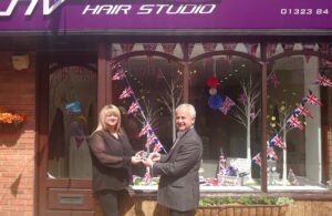 Photo of NV Hair Studio Staff member being presented with the Best Dressed Coronation Window Display award by Deputy Town Clerk and Business Entrprise Manager Mickey Caira